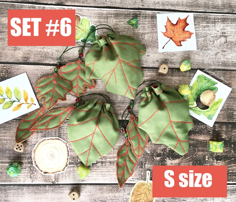 May include: Green leaf-shaped drawstring bags with red vein detailing, labeled "S size" and "SET #6". The bags are accompanied by leaf-shaped embellishments and watercolor illustrations of leaves. Dice are scattered around the bags.