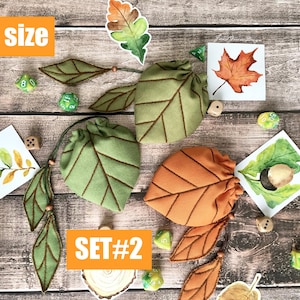 May include: Two leaf-shaped drawstring bags, one green and one orange, with brown stitching, are displayed with leaf-themed embellishments and dice. The text "S size" and "SET#2" are visible. The items are arranged on a wooden surface.