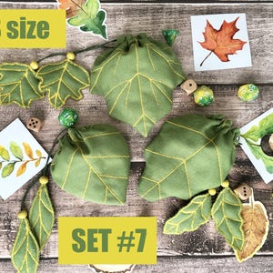 May include: Green leaf-shaped drawstring bags with yellow stitching, accompanied by leaf-themed embellishments and dice. The bags are labeled "S size" and "SET #7". The image has a rustic, autumnal theme.