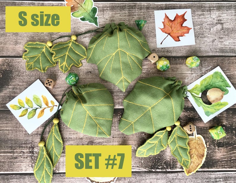 May include: Green leaf-shaped drawstring bags with yellow stitching, accompanied by leaf-themed embellishments and dice. The bags are labeled "S size" and "SET #7". The image has a rustic, autumnal theme.