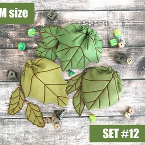 May include: A set of three green leaf-shaped dice bags with brown stitched details. The bags are arranged with several dice on a wooden surface. The text "M size" and "SET #12" are visible.