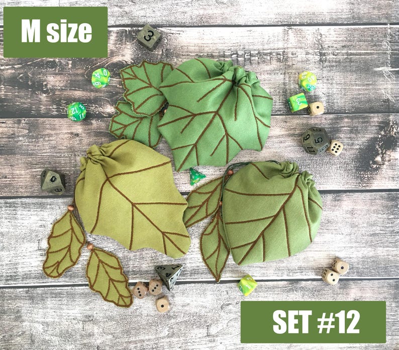 May include: A set of three green leaf-shaped dice bags with brown stitched details. The bags are arranged with several dice on a wooden surface. The text "M size" and "SET #12" are visible.