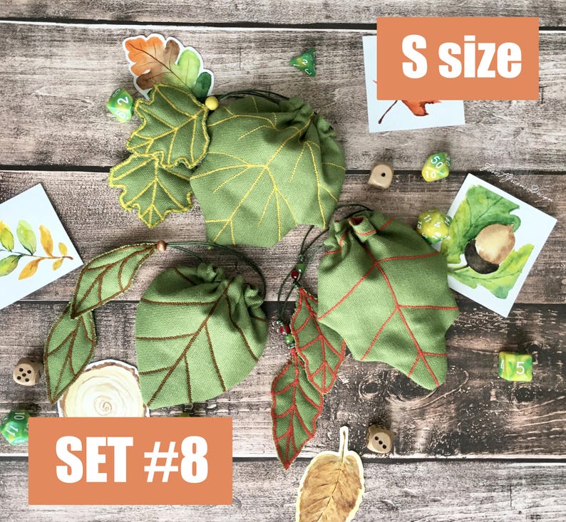 May include: Green leaf-shaped dice bags with yellow and red stitching, and drawstring closures. The bags are labeled "S size" and "SET #8". The image includes dice and leaf-themed artwork on a wooden surface.