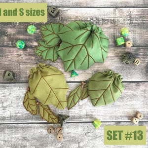 May include: Three green leaf-shaped drawstring bags with brown vein detailing are displayed with several dice. The bags are labeled "M and S sizes" and "SET #13". The dice are in various colors, including green and white.