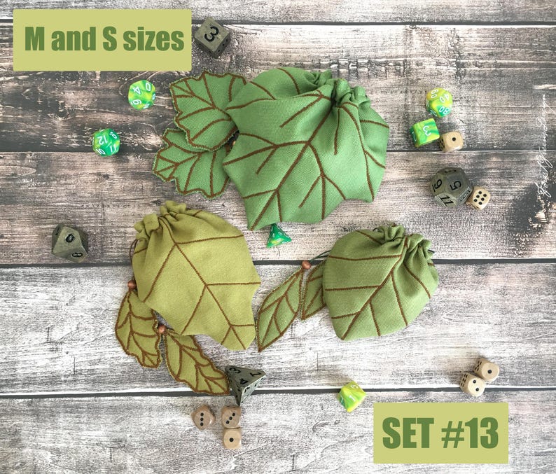 May include: Three green leaf-shaped drawstring bags with brown vein detailing are displayed with several dice. The bags are labeled "M and S sizes" and "SET #13". The dice are in various colors, including green and white.