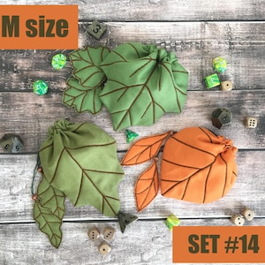 May include: Three leaf-shaped dice bags in green and orange, with brown stitched details. The bags are arranged on a wooden surface with various dice scattered around. The text "M size" and "SET #14" are visible.