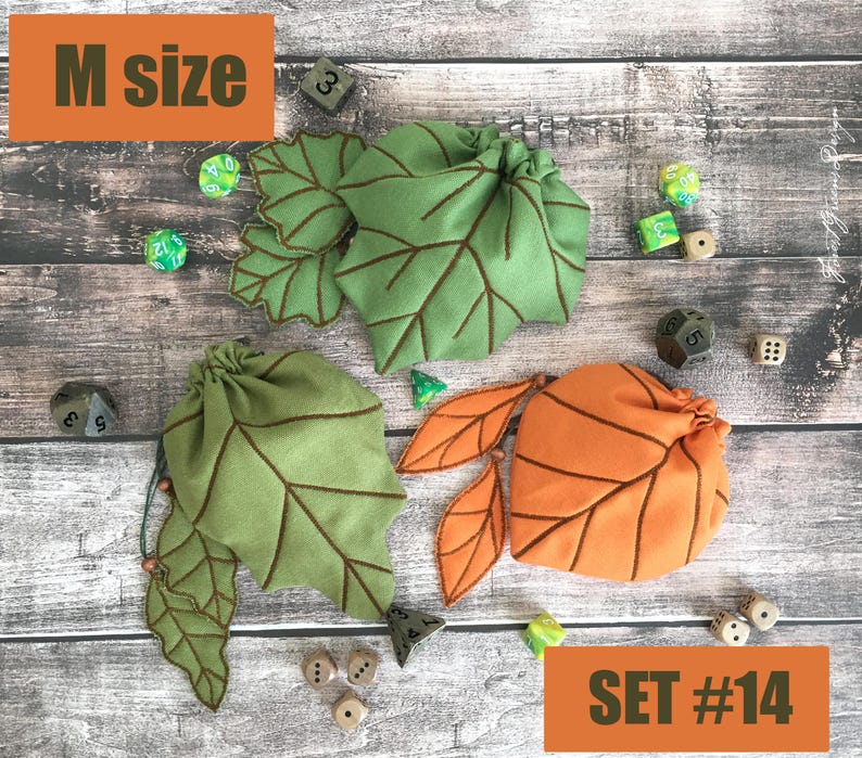 May include: Three leaf-shaped dice bags in green and orange, with brown stitched details. The bags are arranged on a wooden surface with various dice scattered around. The text "M size" and "SET #14" are visible.