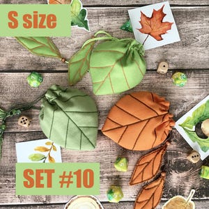 May include: Three leaf-shaped drawstring bags in green and orange, with brown stitching, are displayed on a wooden surface. The bags are accompanied by dice and leaf-themed artwork. The text "S size" and "SET #10" are visible.