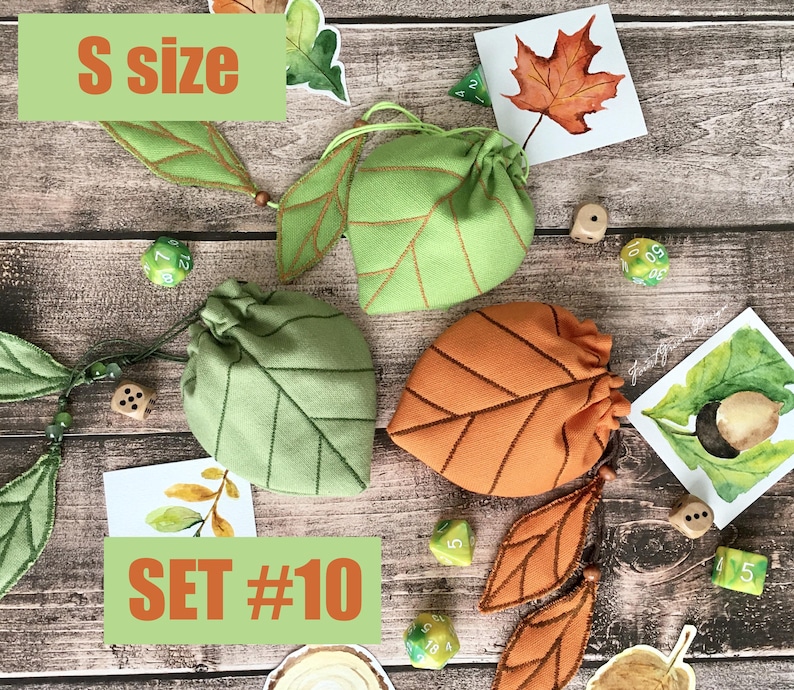 May include: Three leaf-shaped drawstring bags in green and orange, with brown stitching, are displayed on a wooden surface. The bags are accompanied by dice and leaf-themed artwork. The text "S size" and "SET #10" are visible.