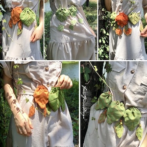 May include: A beige dress with a leaf-themed accessory. The accessory features green and orange leaf-shaped pouches and leaves, connected by a vine. The dress has a button-down design and a ruffled hem.
