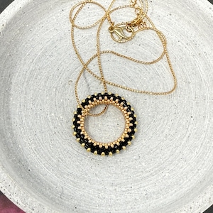 Puede incluir: Un collar de cadena dorada con un colgante circular de cuentas negras y doradas.