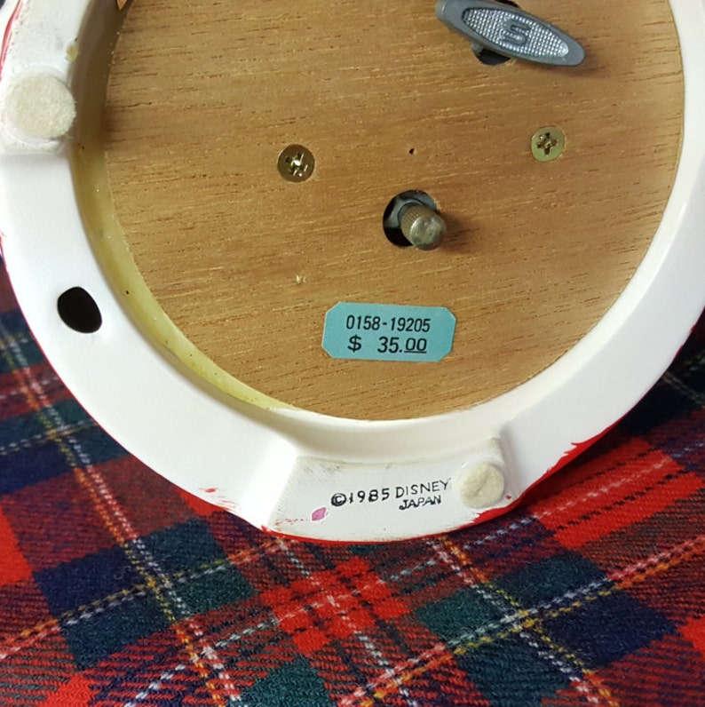 May include: The underside of a ceramic musical figurine with a wooden base. The base has a price tag that reads "0158-19205 $ 35.00". The figurine is marked "&copy;1985 DISNEY JAPAN".