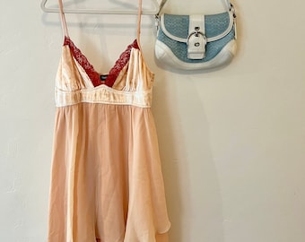 May include: A peach-colored layered dress with a red velvet bodice and lace trim hangs on a white hanger. A light blue and white patterned handbag hangs on a hook above the dress.