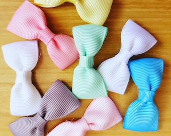 May include: Assortment of eight colorful ribbon bows in various colors, including pink, yellow, white, blue, green, and gray. The bows are arranged in a circular pattern on a wooden surface.