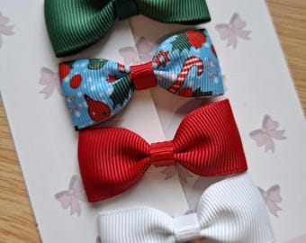 May include: Four colorful hair bows. The top bow is green, the second is blue with a Christmas pattern, the third is red, and the bottom bow is white. The bows are arranged on a white card with the text "Betty's Bow Boutique".