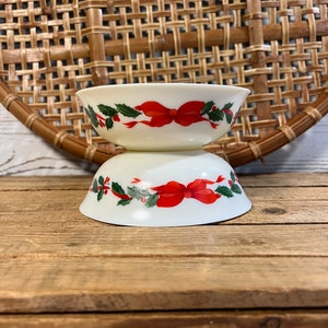 May include: Two white ceramic bowls with a Christmas-themed design. The bowls feature red bows, green holly leaves, and a white background.