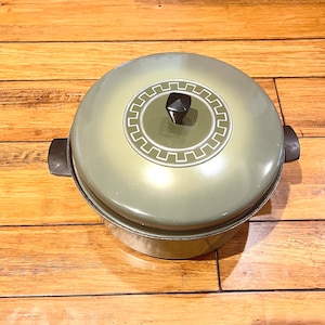 May include: A green ceramic covered casserole dish with a black knob on the lid. The lid has a decorative design with a white circle and a geometric pattern.
