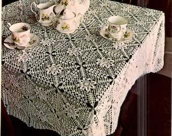 May include: A white crocheted tablecloth with a delicate floral pattern. The tablecloth is laid on a dark wooden table with a teapot, creamer, sugar bowl, and teacups.