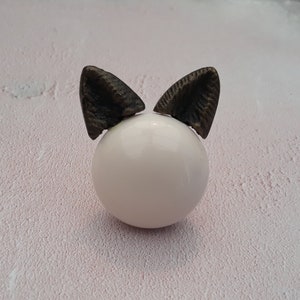May include: White ceramic knob with two dark brown cat ears.