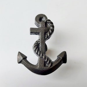 May include: A dark grey anchor with a rope wrapped around the central post. The anchor has a classic design with a ring at the top and two flukes at the bottom. The anchor is made of metal, likely a decorative item.
