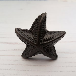 May include: A black cast iron starfish shaped cabinet knob or drawer pull. The starfish has a detailed design with raised lines.