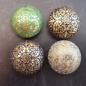 May include: Four round decorative boxes with intricate gold floral designs on different coloured backgrounds. The boxes are green, black, blue, and white.