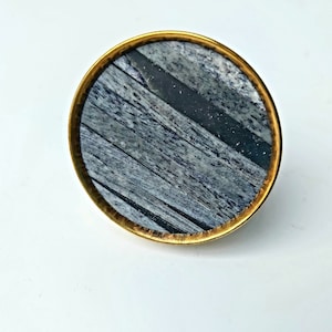 May include: A round, gold-rimmed knob with a grey and black wood-grain pattern.