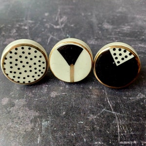 May include: Three round ceramic knobs with black and white geometric designs. The knobs have a gold trim.