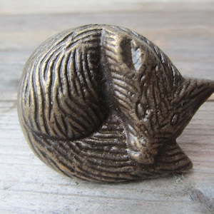 May include: A bronze-coloured metal sleeping fox figurine. The fox is curled up with its tail wrapped around its body. The figurine has a detailed texture and is perfect for adding a touch of whimsy to any home decor.