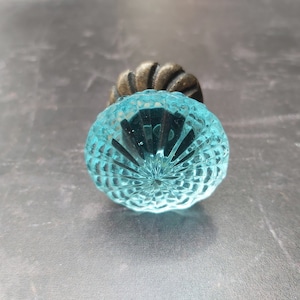 May include: A blue glass cabinet knob with a decorative, faceted design. The knob is attached to a metal base.
