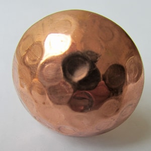 May include: A hammered copper sphere with a smooth, shiny finish. The sphere has a slightly irregular shape and a warm, metallic colour.