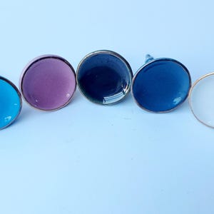 May include: Five ceramic cabinet knobs with a silver rim. The knobs are in the colours blue, purple, dark blue, light blue, and white.