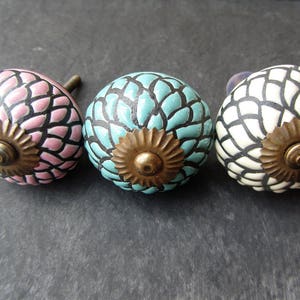 May include: Three ceramic cabinet knobs with a floral design. The knobs are pink, blue, and white with black accents. Each knob has a gold metal centre.
