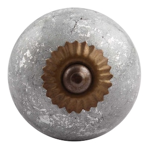 May include: A round, silver-coloured ceramic knob with a gold-coloured metal accent. The knob has a distressed, textured finish.