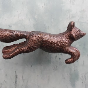 May include: A copper-coloured metal fox figurine in a leaping pose. The fox has a detailed, textured surface and a long, bushy tail.