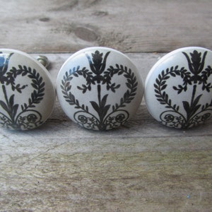 May include: Three white ceramic knobs with black floral designs. The knobs have a slightly raised design and are round.
