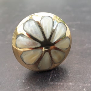 May include: A round, gold-coloured knob with a white, mother-of-pearl inlay in the shape of a flower.
