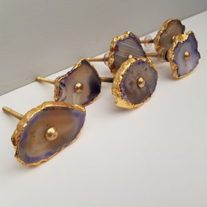 May include: Set of five agate drawer pulls with gold trim. Each pull is a unique shape and features a natural agate stone with purple and brown hues.