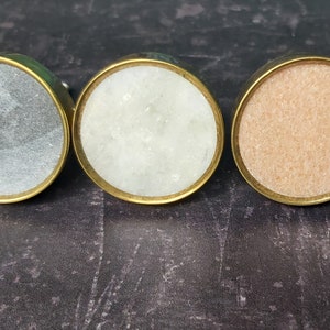 May include: Three round cabinet knobs with a brass rim and a stone inlay. The knobs are grey, white, and light brown.