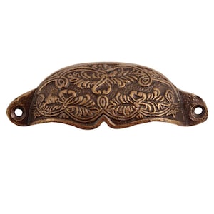 May include: A decorative brass cabinet pull with an ornate floral design. The pull is a half-circle shape and has a slightly aged finish.