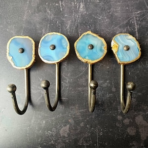 May include: Four blue agate hooks with gold trim and a metal hook. The hooks are mounted on a dark grey wall.