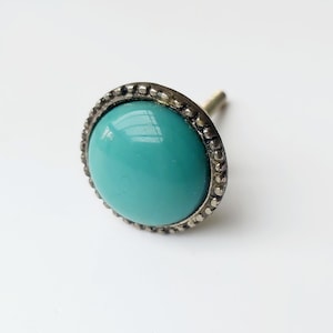 May include: A turquoise blue glass knob with a silver metal rim and a decorative beaded edge. The knob has a screw on the back for attaching to a drawer or cabinet.
