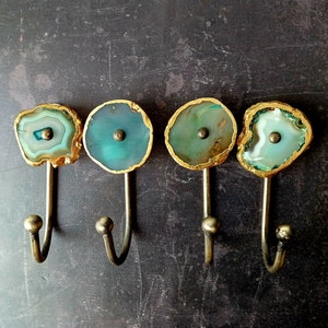 May include: Four gold-rimmed agate hooks with a blue-green and white pattern. Each hook has a rounded top and a metal hook.