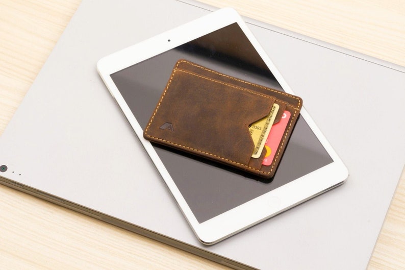 May include: A brown leather wallet with a flap and a credit card inside, sitting on top of a silver laptop.