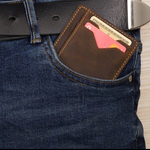 May include: A brown leather wallet with a flap pocket and a credit card inside. The wallet is in a blue jean pocket.