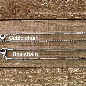 May include: Two silver chains on a wooden surface. The top chain is labelled "Cable chain" and the bottom chain is labelled "Box chain".
