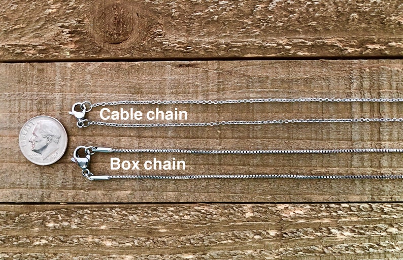 May include: Two silver chains on a wooden surface. The top chain is labelled "Cable chain" and the bottom chain is labelled "Box chain".