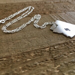 May include: Silver necklace with a pendant shaped like the state of Arizona featuring a small cactus design.