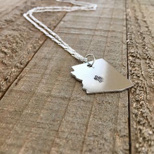 May include: A silver necklace with a pendant shaped like the state of Arizona featuring a small cactus design in the centre.