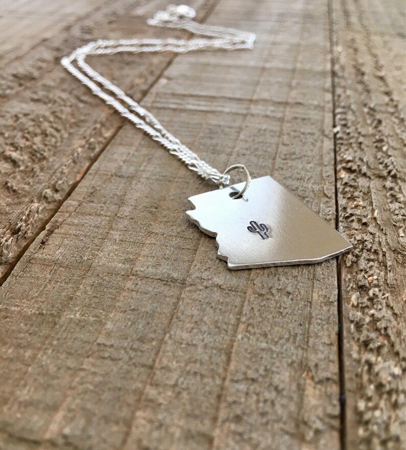 May include: A silver necklace with a pendant shaped like the state of Arizona featuring a small cactus design in the centre.